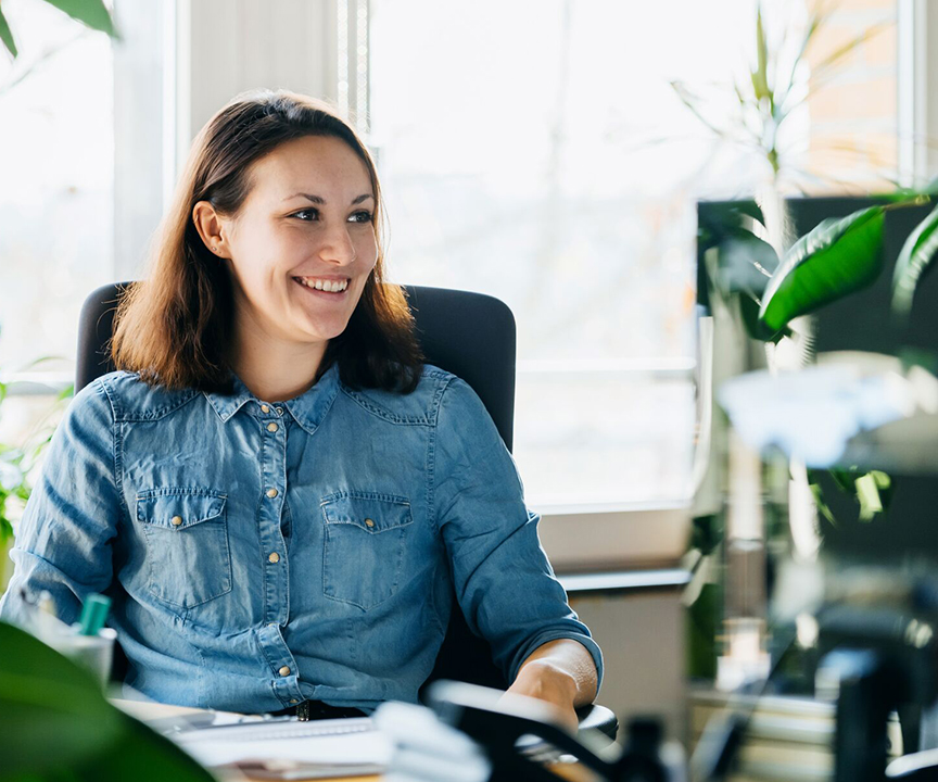 Blije vrouw die aan haar bureau zit en op een computer werkt